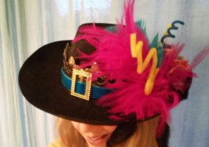 Visage caché sous un chapeau avec plumes et accessoires illustrant la Maison Dieu